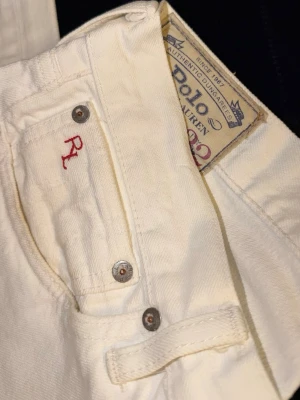 Vita jeans från Polo Ralph Lauren - Säljer ett par klassiska vita jeans från Polo Ralph Lauren. De har en rak passform, fem fickor och snygga metallnitar. På myntfickan finns en röd RL-brodering som extra detalj. Perfekta till en clean och stilren look. 31/32
