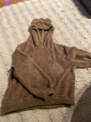 Brun teddy hoodie med öron - Mysig brun teddy hoodie från SHEIN med fluffigt material och huva med söta öron. Perfekt för dig som gillar en chill och gullig stil. Tröjan har långa ärmar och avslappnad passform. Materialet är supermjukt och värmande.
