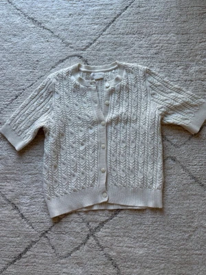 Krämvit stickad kofta  - Krämvit stickad kofta med halvlånga ärmar från Holly & Whyte. Passar storlek S och storlek M. 