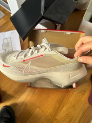 Nike vita mesh sneakers - Säljer ett par vita Nike sneakers med mesh-överdel och tjock sula. Snygga detaljer i rött och genomskinliga partier på sidan. Skorna har klassisk Nike Swoosh och vita skosnören. Perfekta för dig som gillar sportig och modern stil.