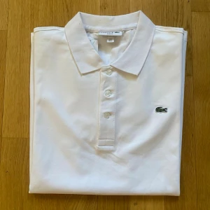 Vit pikétröja från Lacoste - Lacoste Slim Fit Pikétröja i mycket fint skick. Klassisk och stilren modell med smal passform som sitter snyggt på kroppen. Tillverkad i högkvalitativ bomull som är både bekväm och andas bra.   • Storlek: L • Färg: Vit • Skick: Mycket bra, oanvänd   • Nypris: ca 1.200 kr • Pris: 600 kr    Skickas samma arbetsdag! Alltid noggrant paketerad. Hör av dig vid frågor och bilder! Smidiga affärer uppskattas alltid.
