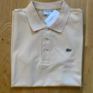 Beige pikétröja från Lacoste - Lacoste Slim Fit Pikétröja i mycket fint skick. Klassisk och stilren modell med smal passform som sitter snyggt på kroppen. Tillverkad i högkvalitativ bomull som är både bekväm och andas bra.   • Storlek: M • Färg: Beige • Skick: Mycket bra, oanvänd   • Nypris: ca 1.200 kr • Pris: 600 kr    Skickas samma arbetsdag! Alltid noggrant paketerad. Hör av dig vid frågor och bilder! Smidiga affärer uppskattas alltid.