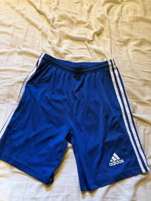 Blå Adidas shorts med vita ränder - Blåa Adidas shorts, knappt använda. Storlek 176 (barn) 