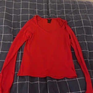 Röd långärmad topp från Lindex - Säljer en röd långärmad topp från Lindex i storlek S. Toppen har en lätt ribbad struktur och v-ringad halsringning. Perfekt att styla med jeans eller kjol för en snygg och enkel look.