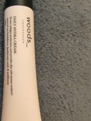 Woods Copenhagen Daily Hydra Cream - Fuktgivande ansiktskräm från Woods Copenhagen i en vit tub med svart lock. Daily Hydra Cream boostar kollagenproduktionen och ger intensiv återfuktning med hyaluronsyra och antioxidanter. Perfekt för daglig hudvård.