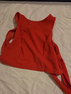 Röd croppad linnetopp med knyt - Trendig röd croppad linnetopp med breda axelband och knyt i sidan. Perfekt för dig som vill ha en enkel men snygg topp till sommaren. Tillverkad i mjuk bomull som känns skön mot huden.