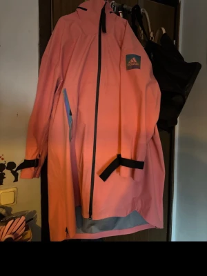 Rosa regnjacka från Adidas - Snygg rosa regnjacka från Adidas med svart dragkedja och detaljer. Jackan har huva, längre passform och logga på ärmen. Tillverkad i vattenavvisande material, perfekt för regniga dagar. Justerbara muddar med kardborreband för extra komfort. ( se bild för fläckar ) passar L - XL skulle jag säga :) 