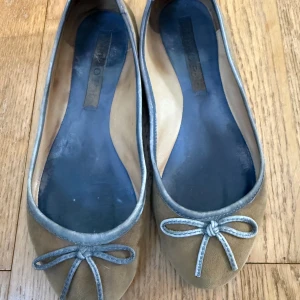 Beige ballerinaskor med rosett - Snygga ballerinaskor från Marc O’Polo i beige mocka med rund tå och dekorativ rosett framtill. Skorna har en tunn sula och en enkel, klassisk design som passar till många olika stilar. Perfekta för dig som gillar minimalistiskt mode.  Stl 36, fint skick  Nypris ca 1600kr