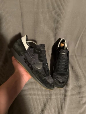 Pkilippe model  - Snygga svarta sneakers från Philippe model med camo-mönster i textil och mocka. Skorna har svarta skosnören, svart sula och en kontrasterande vit detalj vid hälen. Perfekta för dig som vill ha en stilren men ändå unik look.