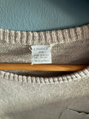 Beige t-shirt från Lindex Kids - En enkel och stilren beige t-shirt från Lindex Kids. T-shirten har korta ärmar, rund halsringning och är gjord i ett mjukt material som känns skönt mot huden. Perfekt till alla dina outfits och lätt att matcha med andra plagg.