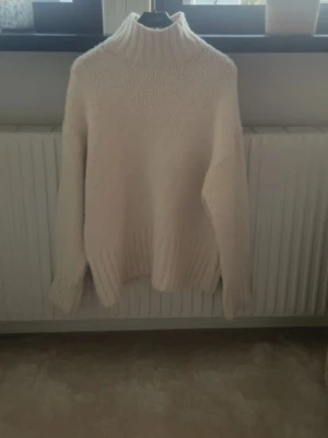 Vit stickad polotröja från H&M - Mysig vit stickad polotröja från H&M i storlek XS. Tröjan har en hög polokrage, långa ärmar och breda ribbade muddar vid ärmslut och nederkant. Perfekt för kalla dagar och enkel att matcha med olika outfits.