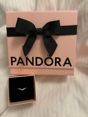 Pandora silverring i V-form - Säljer en stilren silverring från Pandora i V-form. Ringen är tunn och elegant, perfekt för att kombinera med andra ringar eller bära ensam. Kommer i original rosa ask med svart rosett och presentkort. Den är väl använd med fortfarande i ett bra skick. Den kostar 400 kr ny pris men eftersom att den har använts flitigt säljer jag den för 199 kr. Ringen är i storlek 58 av pandoras storlekar, jag hänvisar till pandoras hemsida för storleksguide.