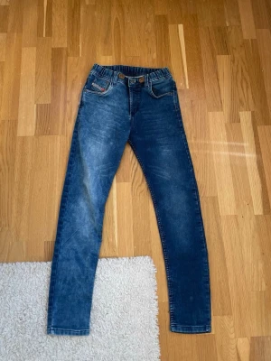 Mörkblå skinny jeans med stretch - Snygga mörkblå skinny jeans med lätt slitning och stretchig midja. Klassisk femficksmodell med kontrastsömmar och smal passform. Perfekta till vardagslooken och enkla att matcha med olika stilar.