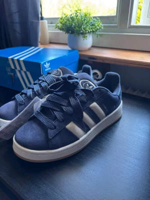 Adidas Campus 00 Marinblåa - Adidas Campus 00 Helt nya – aldrig använda (lapp kvar) Strl 38 (junior) 🔹 Mörkblå/vit 🔹 Extra vita snören ingår 🔹 Trendig & clean modell Säljes då det är för små så testar här!