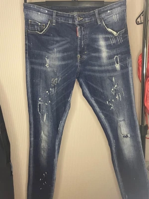 Dsquared2 - Snygga mörkblå jeans med slitningar och vita färgstänk för en trendig, avslappnad look. Jeansen har raka ben, klassisk femficksdesign och tydliga slitdetaljer framtill. Perfekta för dig som gillar streetstyle och vill sticka ut. Storlek 50 hör av er vid frågor:) endast  349:- !!