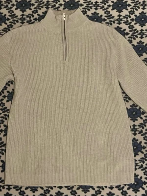 ribbstickad tröja med halvzip - En ribbad tröja i storlek L i färgen grey melange. Den är använd ett fåtal gånger och är i nästan nyskick. Jag har haft den i ungefär två månader men säljer den eftersom den är för stor för mig. Tröjan har en mjuk ribbstickad struktur och en enkel, stilren design. 