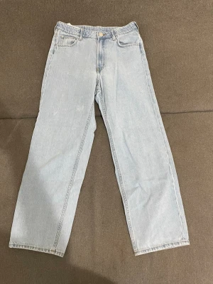 Ljusblå raka jeans i denim - Säljer ett par ljusblå jeans med rak passform och klassisk femficksdesign. Jeansen har hög midja och stängs med knapp och dragkedja. Tillverkade i denim, perfekta för en avslappnad och trendig look.