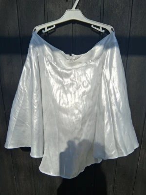 Silverfärgad kjol med glansig finish - Säljer en glansig silverfärgad kjol i silber metallic. Tyget har en skimrande yta som ger en magisk känsla och aldrog använd. Stängs med dragkedja bak.