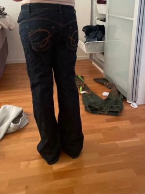 Mörkblå bootcut jeans med kontrastsömmar - Säljer ett par mörkblå bootcut jeans med snygga kontrastsömmar och broderade bakfickor. Jeansen har klassisk femficksdesign och är tillverkade i denim. Perfekta för dig som gillar en avslappnad men ändå trendig look.