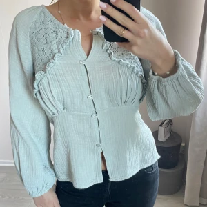 Ljusgrön blus med spetsdetaljer - Supersöt ljusgrön blus med knappar framtill, lång ärm och fina virkade spetsdetaljer vid axlarna. Storlek 13-14 år, ca XS-S. Sytt om vissa detaljer själv, därav pris och sömmar.