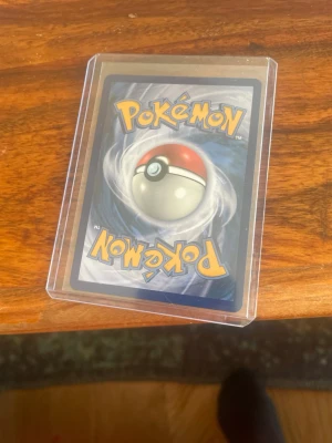 Pokémonkort Aurorus i plastfodral - Säljer ett Pokémonkort med Aurorus-motiv, innesluten i ett genomskinligt plastfodral. Kortet har en blå baksida med klassisk Pokéball och framsidan visar Aurorus med 170 HP och attacker som Tundra Wall och Freezing Chill. Perfekt för samlare eller Pokémonfans.