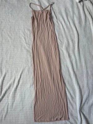 Beige långklänning med smala axelband - Säljer en stilren beige långklänning med smala axelband och figurnära passform. Klänningen har en enkel design utan mönster och är tillverkad i ett mjukt, stretchigt material som känns bekvämt mot huden. Perfekt för dig som gillar minimalistisk stil!💓🌸