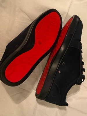 Svarta Christian Louboutin sneakers - Snygga blåa sneakers från Christian Louboutin med klassisk röd sula och diskreta metalldetaljer. Skorna har lågt skaft och är tillverkade i mocka med blå snören och blå öglor. Perfekta för dig som vill ha en exklusiv och stilren look.