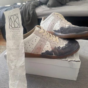 Maison Margiela gats - Öppen för byten mot kläder och skor, kan träffas i Sthlm. Öppen för prisförslag! Maison Margiela sneakers i vitt och grått med coolt prickigt mönster och mörka färgdetaljer på tån. Skorna har beige snörning, gummisula i brunt och paneler i mocka och skinn. Storlek 42, kvitto finns! Har tyvärr inte kvar lådan, köpte de av någon annan utgår från det han sa och från kvittot. Sulorna är som killen skickade skorna med är lite konstiga men jag utgår fortfarande från att de är äkta.