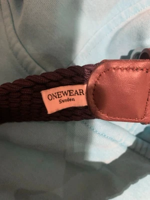 Mörkblått flätat bälte från ONEWear - Snyggt mörkblått flätat bälte från ONEWear Sweden med bruna skinn-detaljer och silverfärgat spänne. Perfekt accessoar för att lyfta din outfit och passar till både jeans och chinos. Bältet är 90 cm långt.