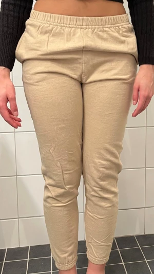 Beige mjukisbyxor med resår - Säljer ett par beige mjukisbyxor med resår i benslut och midja. Byxorna har en smal passform och är tillverkade i ett mjukt och stretchigt material som känns skönt mot huden. Perfekta för chill dagar hemma eller när du vill ha det bekvämt.