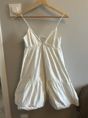 Vit sommarklänning med tunna band - Söt vit klänning med tunna axelband och v-ringning. Klänningen har volangdetaljer och snörning i ryggen för en extra söt look. 