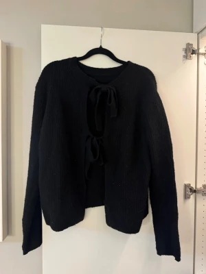 Svart stickad kofta med två knyten - Svart stickad kofta med knytband framtill. Mjuk och skön med avslappnad passform. Enkel att matcha och passar till det mesta.😙💕 (finns ingen lapp på tröjan men är från Nelly i storlek S)!! 