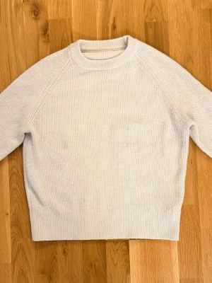 Vit stickad tröja - Dazy - En stilren vit stickad tröja med rund halsringning och långa ärmar. Tröjan har en enkel, ribbstickad struktur och raka muddar vid ärmslut och nederkant. Perfekt för lager på lager och passar till det mesta i garderoben. Obs! Har ett par fläckar, därav priset. 