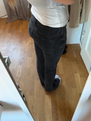 Svarta bootcut jeans med låg midja - Säljer ett par svarta bootcut jeans med hög midja och klassiska bakfickor. Jeansen har en snygg tvättad look och stängs med knapp och dragkedja. Perfekta för dig som gillar en avslappnad men trendig stil.