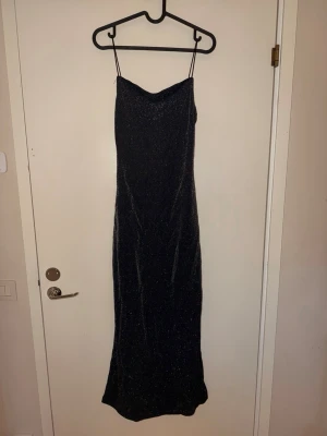 Svart glittrig långklänning - Säljer en svart långklänning med tunna axelband och glittrigt tyg. Klänningen har en figurnära passform med mer ”flow” vid benen.