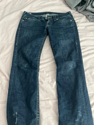 Mörkblå jeans True Religion - Säljer ett par mörkblå raka jeans från True Religion med klassiska kontrastsömmar och snygga fickdetaljer bak. Jeansen har låg midja och är tillverkade i slitstark denim med en cool tvätt. Perfekta för dig som gillar en avslappnad men trendig stil.