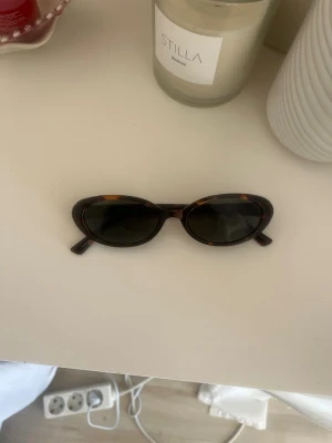 Bruna runda solglasögon i plast - Snygga solglasögon med rund form och klassiskt brunt sköldpaddsmönster. Bågarna är tillverkade i plast och ger en trendig retrovibe. Perfekta för dig som vill ha en stilren accessoar till sommaren.