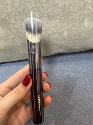 Hourglass foundation sminkborste med syntetborst  - Lyxig foundation sminkborste från Hourglass med tätt, mjukt syntetborst i vitt och grått. Handtaget är mörkbrunt med metallisk finish och har Hourglass-loggan i guld. Perfekt för applicering av foundation eller puder. Borsten har en rundad form för jämn applicering. Kostade 729 på sephora