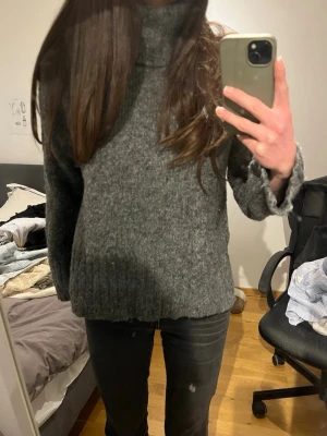 Grå stickad polotröja - Mysig grå stickad polotröja med hög krage och avslappnad passform. Tröjan har långa ärmar och ribbstickade muddar vid ärmslut och nederkant. 