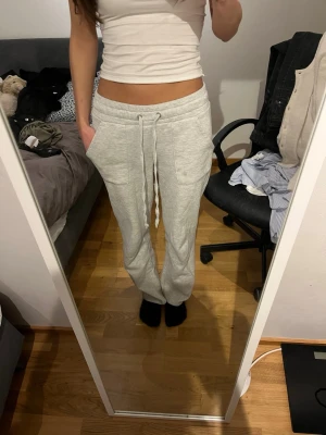 Ljusgrå mjukisbyxor med dragsko - Säljer ett par ljusgrå mjukisbyxor med raka ben och bred resår i midjan. Byxorna har snörning framtill och två stora fickor på sidorna. 