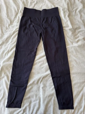 Svarta leggings med strukturdetaljer - Säljer ett par svarta leggings med hög midja och snygga strukturdetaljer längs benen. De är stretchiga och har en tight passform som framhäver benen. Perfekta för dig som vill ha både stil och komfort i vardagen.