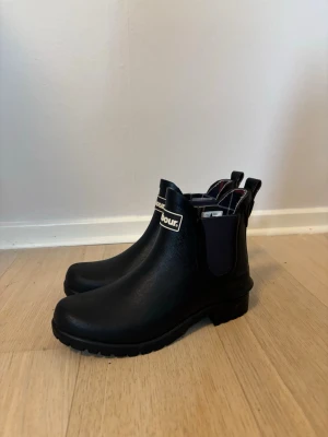Låga stövlar från Barbour - Snygga mörkblåa gummistövlar från Barbour med klassiskt rutigt foder på insidan. Stövlarna har en låg modell och tydlig Barbour-logga bak. Gjorda i gummi✨