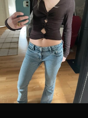 Brun topp - Trendig brun croppad topp med lång ärm. Toppen har v-ringning och öppna partier. Perfekt för dig som vill sticka ut och matcha med höga jeans eller kjol. 