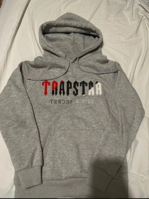 Grå hoodie från Trapstar med tryck - Säljer min trapstar hoodie för har ingen användning till den, den är perfekt skick passar även m