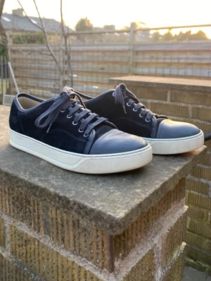 Lanvin skor - Säljer ett par lanvin dbb1 sneakers i storlek uk6 vilket passar 41-42 då det är rätt så breda. Skorna är navy blå och är matta på tån. Mockan är i rätt bra skick och sulan knappast sliten. Extra skosnören följer med vid köp, nypris ligger runt 4000kr👍