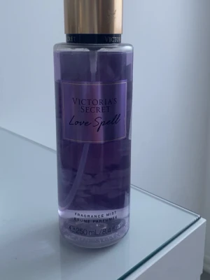 Victoria's Secret Love Spell mist - En snygg parfymmist från Victoria's Secret i doften Love Spell. Flaskan är cylindrisk, genomskinlig med lila vätska och har ett guldigt lock. Rymmer 250 ml och är perfekt att ha med i väskan. Ger en fräsch och söt doft.