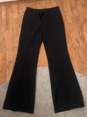 Mörkblå kostymbyxor med vita ränder - Snygga mörkblå kostymbyxor från Gina Tricot med smala vita kritstrecksränder. Byxorna har vida ben och klassisk passform med dragkedja och knapp framtill. Perfekta för en stilren look. Materialet känns mjukt och följsamt.