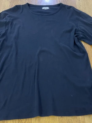 Svart basic t-shirt från KappAhl - En enkel svart t-shirt från KappAhl i storlek L. T-shirten har rund halsringning och korta ärmar. Tillverkad i mjukt bomullstyg som känns skönt mot huden. Perfekt att matcha med jeans eller shorts för en clean och stilren look.