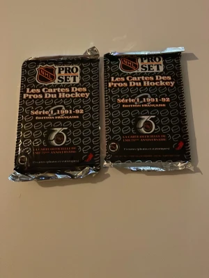 NHL Pro Set hockeykort 1991-92 oöppnade - Två oöppnade paket NHL Pro Set hockeykort från säsongen 1991-92, fransk version. Svarta förpackningar med silverdetaljer och NHL-logga. Perfekt för samlare eller dig som gillar retro sportprylar.