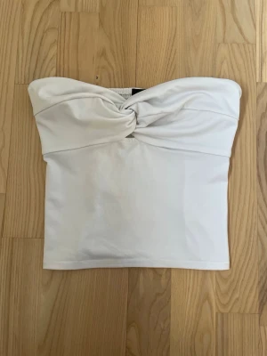 Vit bandeau tubtopp med twist - Snygg vit bandeau tubtopp med twistad detalj framtill och smockad baksida för extra komfort. 